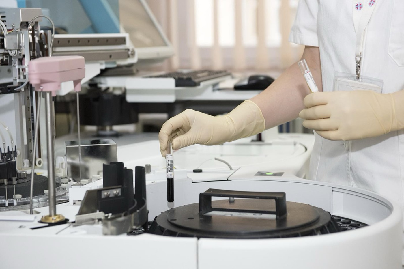 Mãos enluvadas posicionando um tubo de coleta em uma centrífuga de laboratório